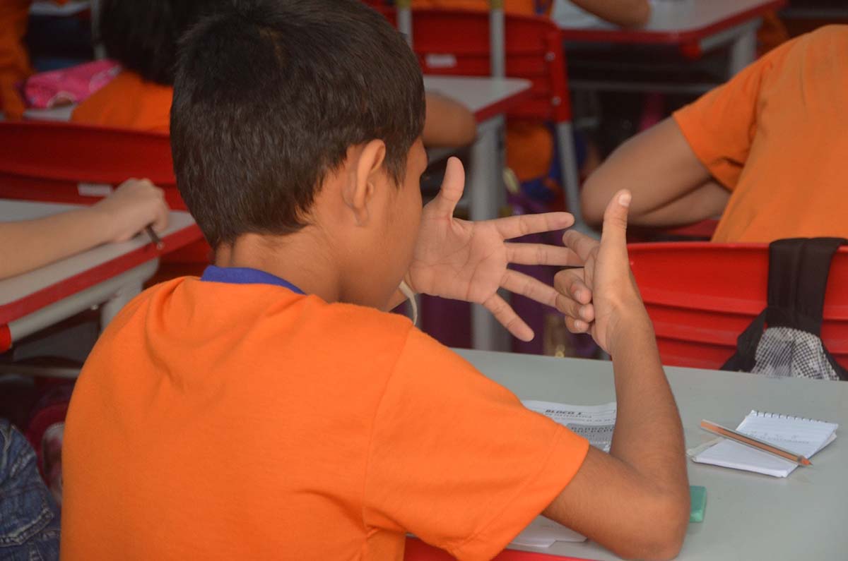 A boy in an orange t-shirt counting on his fingers.